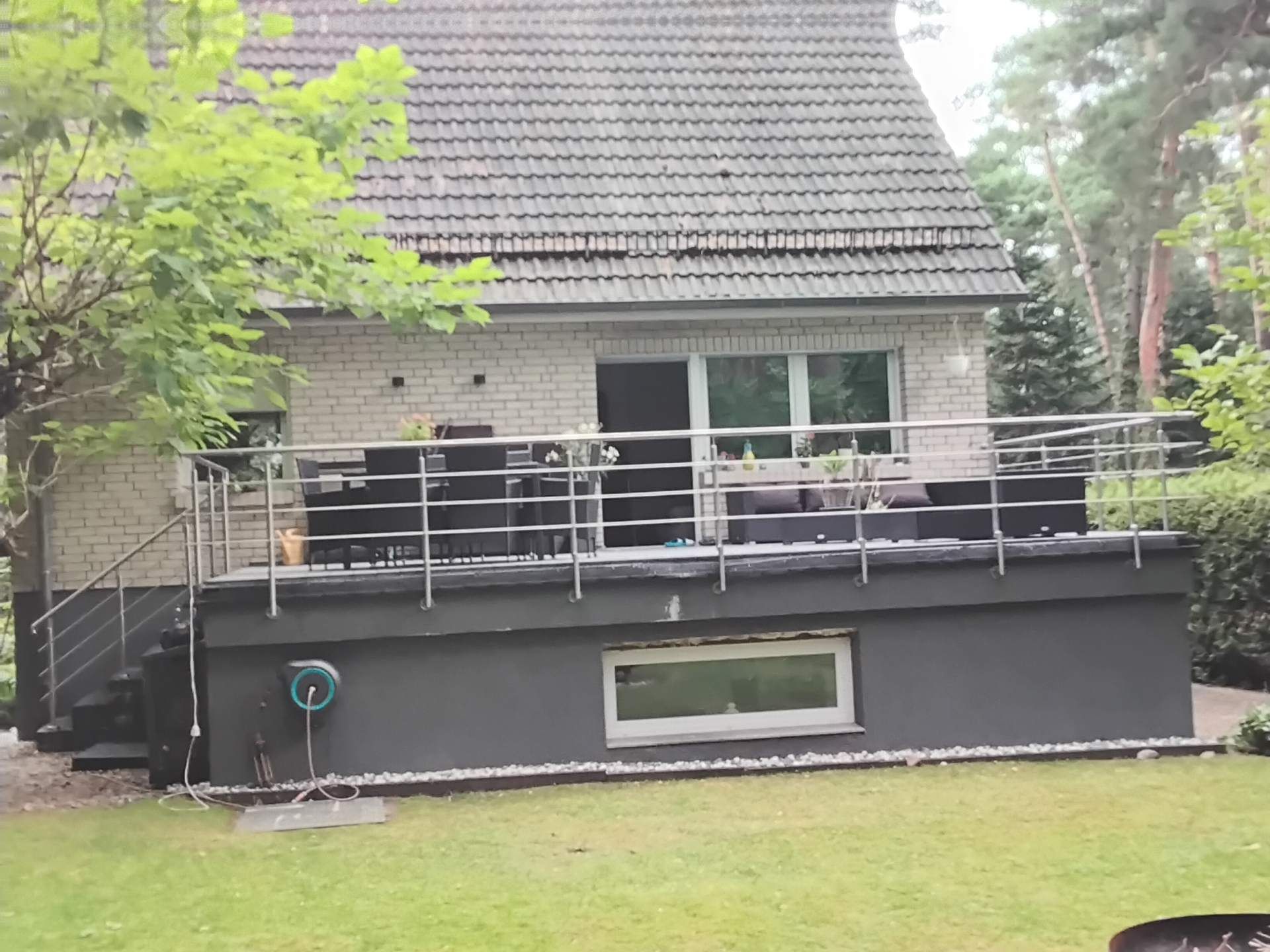 Langer Balkon mit Edelstahlgeländer entlang einer Hausfassade im Garten