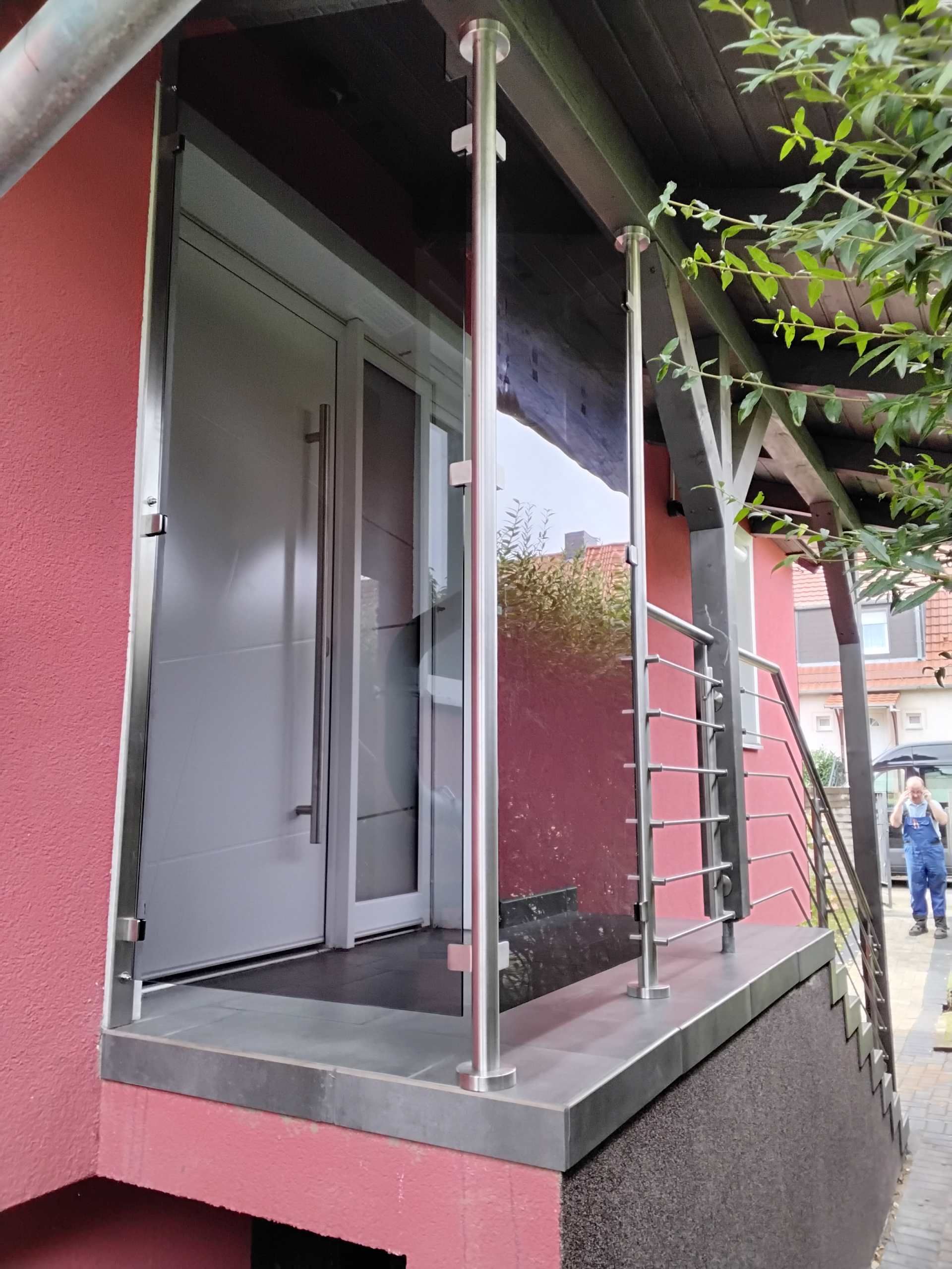 Balkon oder Laufsteg mit Edelstahlgeländer entlang einer roten Hausfassade