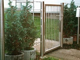 Modernes Gartentor aus Metall mit senkrechten Stäben zwischen Hecken