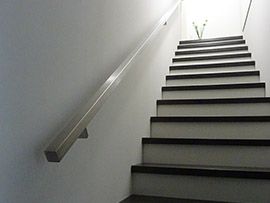 Innenliegende Treppe mit schlichtem Edelstahlhandlauf an Wand