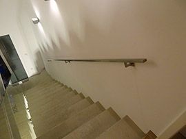 Gerade Innentreppe mit Edelstahlhandlauf an heller Wand