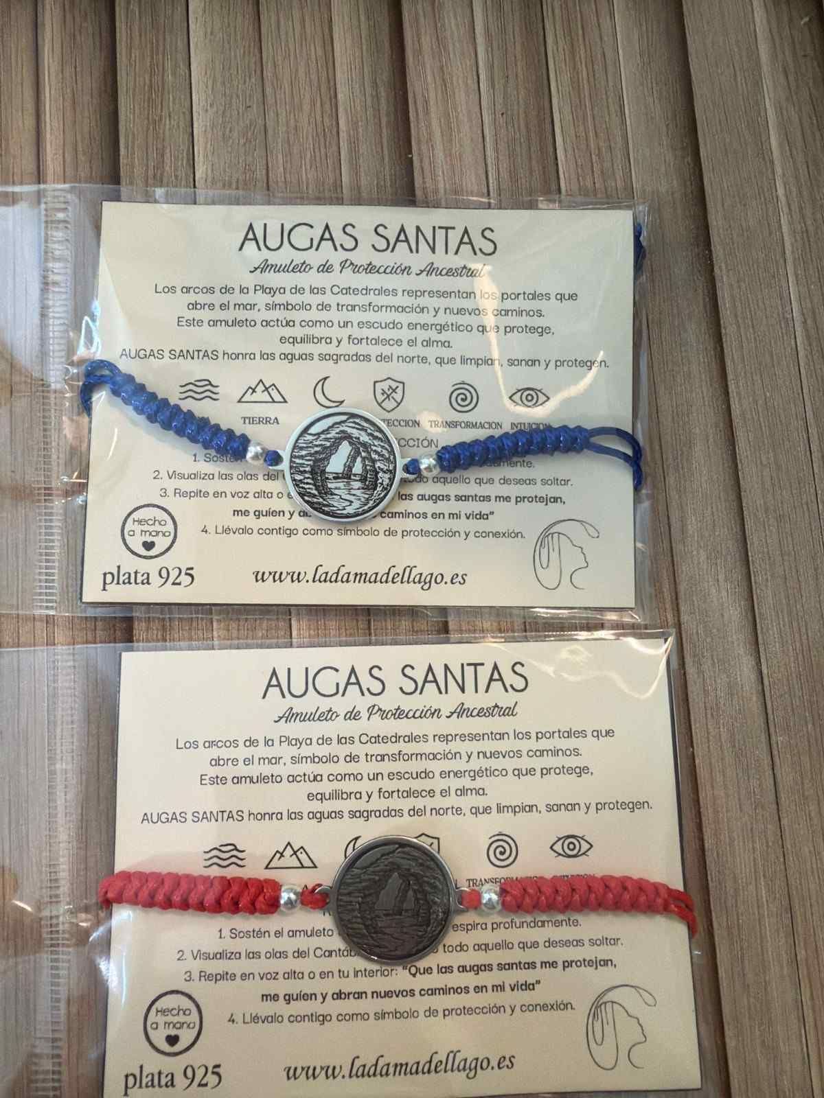 Dos pulseras empaquetadas con la etiqueta “AUGAS SANTAS”, una azul y otra roja, sobre una superficie de madera.