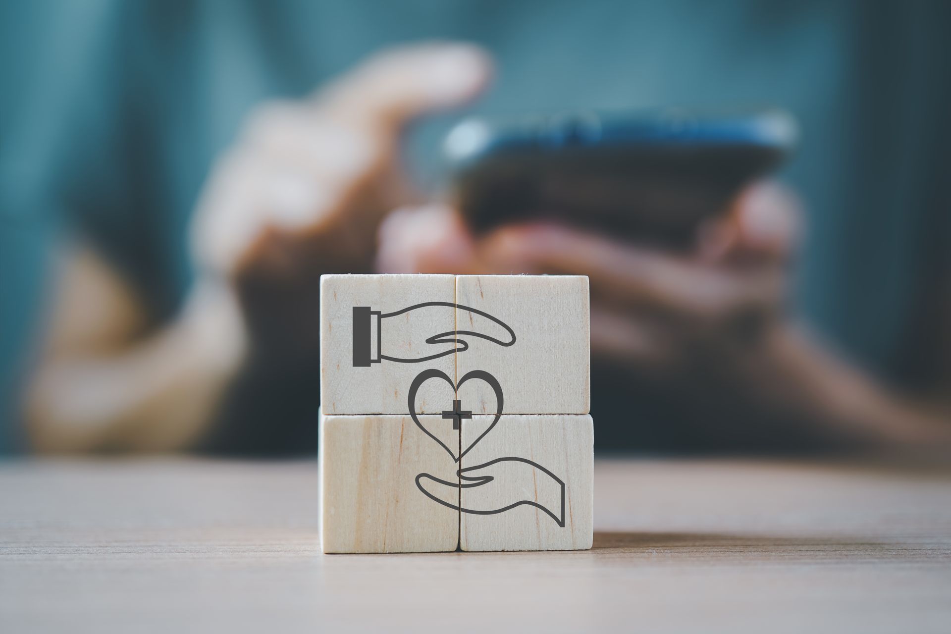 Blocs de bois avec symbole d'un cœur et une croix entre deux mains, tenus devant une personne utilisant un smartphone.
