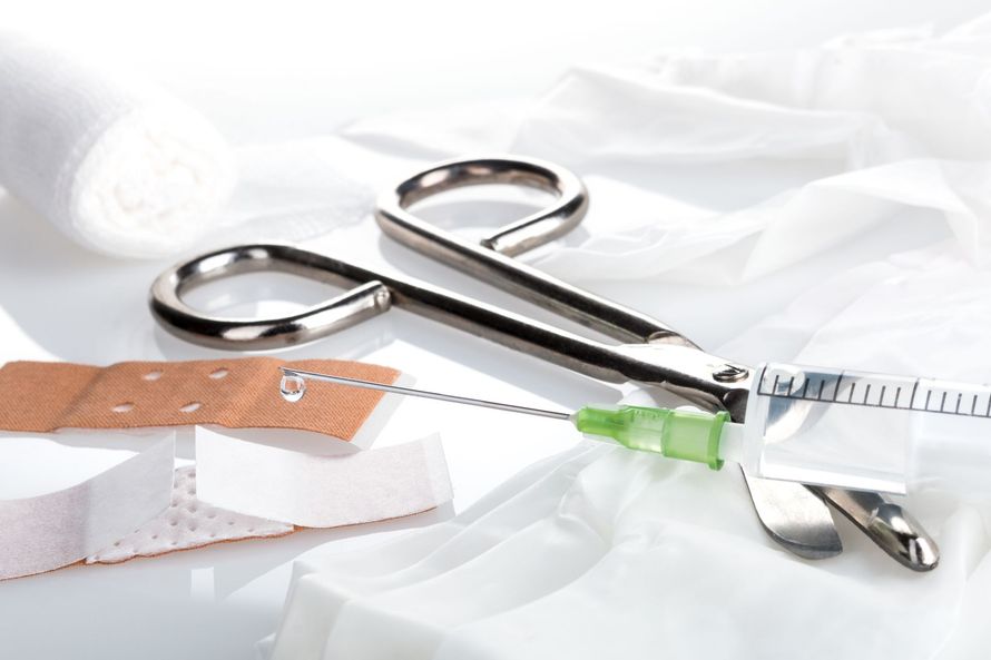 Des ciseaux médicaux, une seringue, des bandages et un rouleau de gaze posés sur une surface recouverte d'un drap blanc.