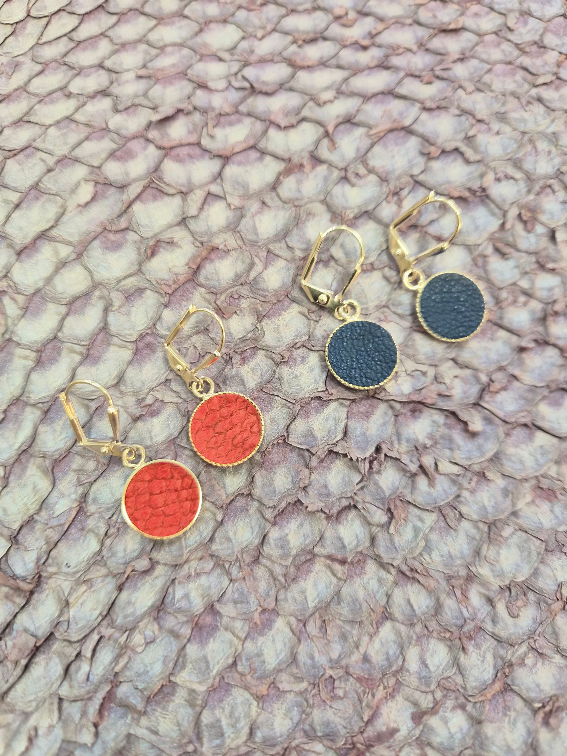 Boucles d'oreilles pendantes dorées avec pendentifs en coquillage violet irisé sur fond de coquillage.