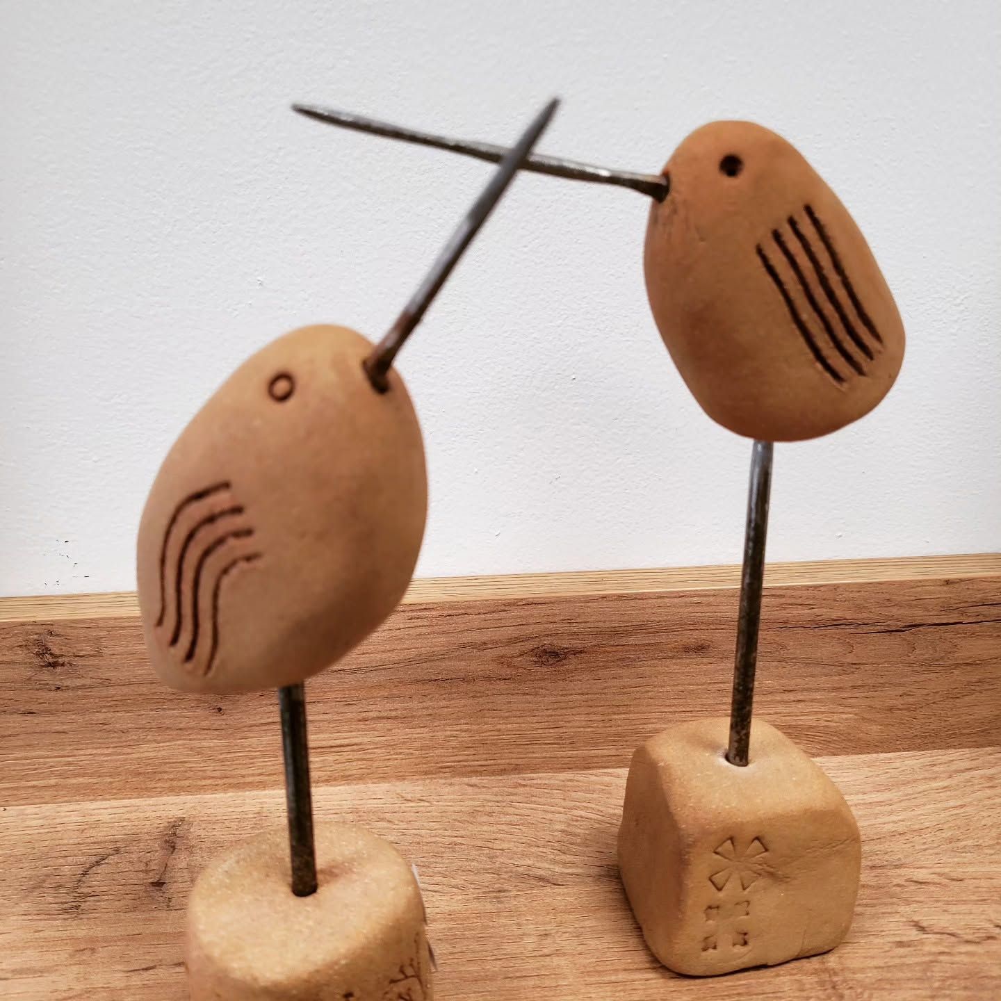 Deux figurines d'oiseaux en céramique sur des blocs, face à face, becs croisés.