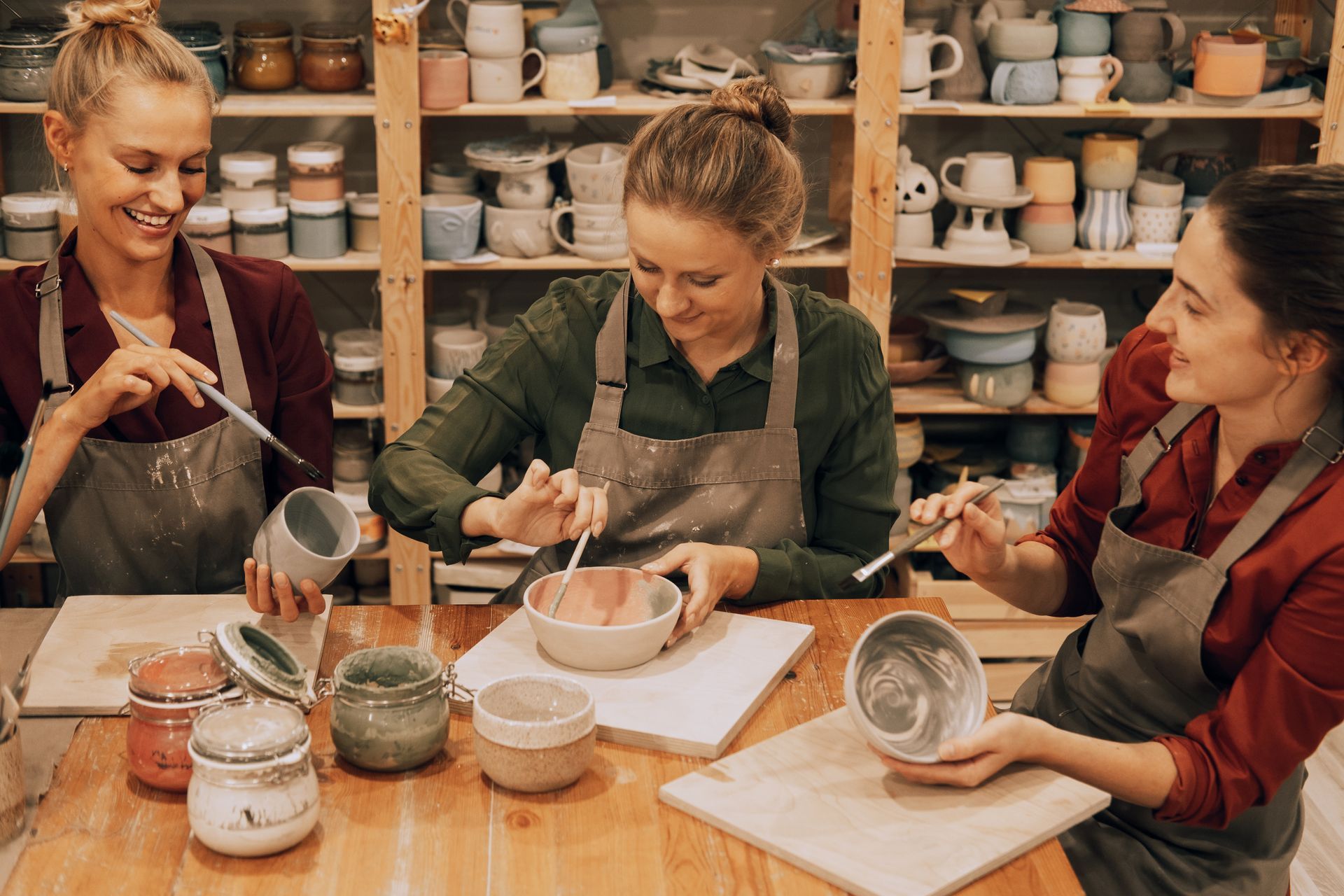 Dans un atelier de céramique, trois personnes peignent des poteries à une table et maniant pinceaux et pièces de céramique.