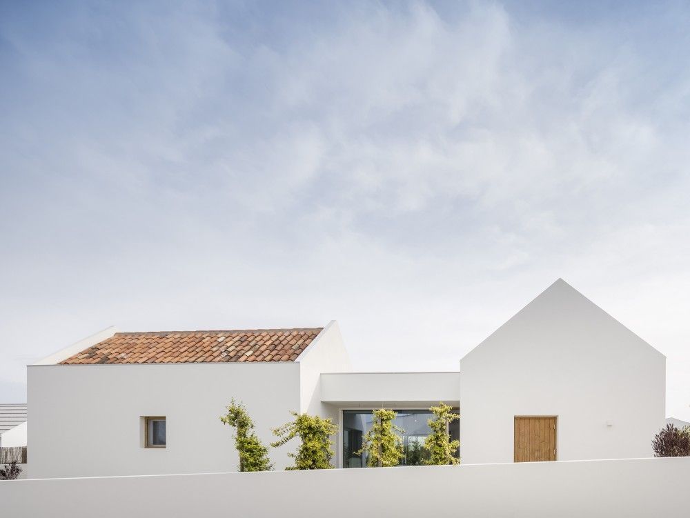 Casa moderna blanca con techo de terracota, pequeños árboles y cielo azul.