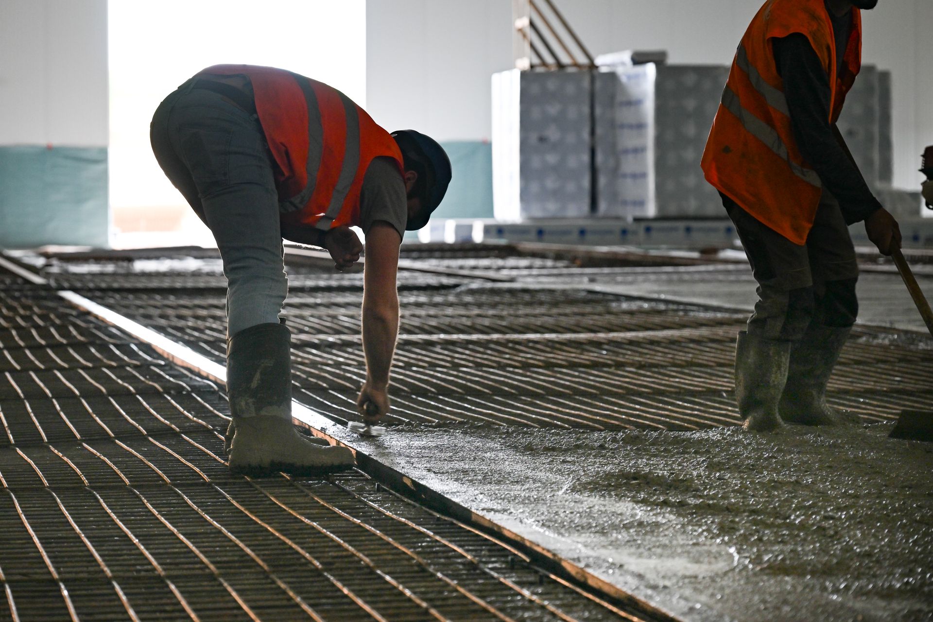 Bras articulé rouge pour couler une dalle en béton dans un hangar agricole.