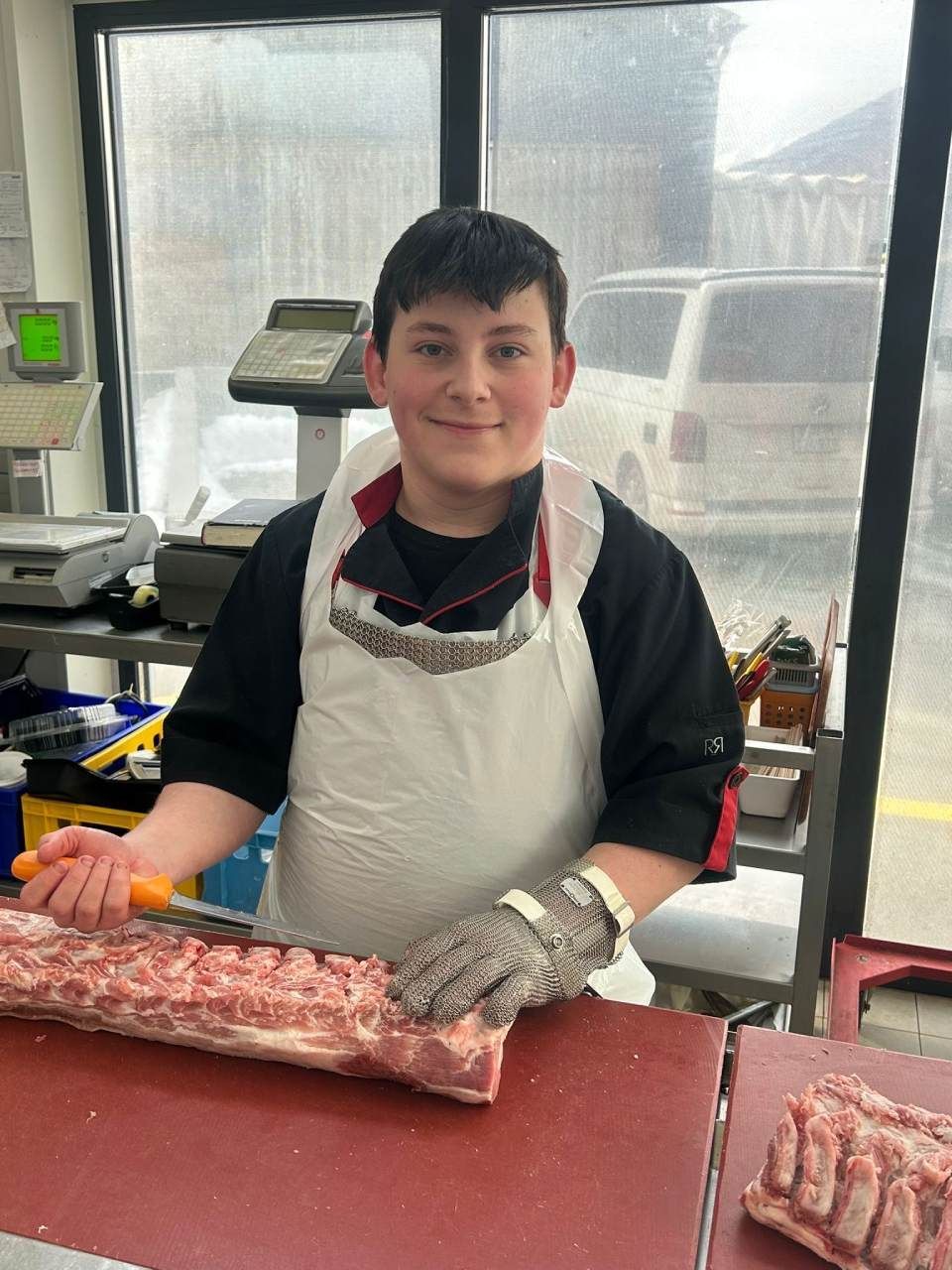 Une personne vêtue d'une tenue de boucher découpe de la viande à un comptoir, en souriant.