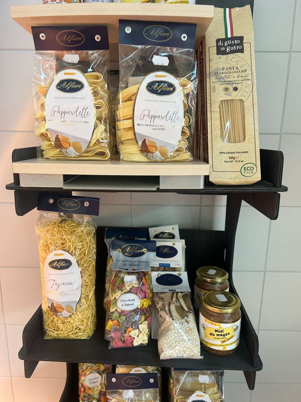 Des pâtes et des bocaux sont présentés sur une étagère en bois à plusieurs niveaux dans un magasin.