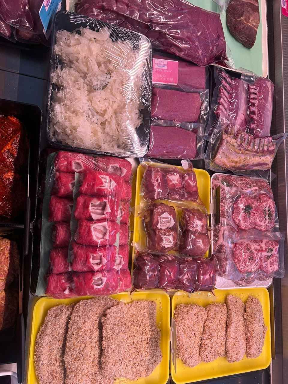 Vitrine à viande présentant diverses coupes de viande crue, principalement rouge, emballées sur des plateaux jaunes.