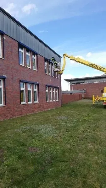 Eine Person in einem gelben Gabelstapler arbeitet an der Seite eines roten Backsteingebäudes mit dunkelgrauem Dach.