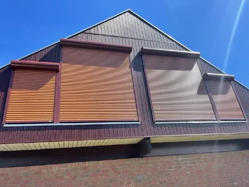 Braune Fensterläden an einem braun-beigen Gebäude mit dreieckigem Dach unter klarem, blauem Himmel.