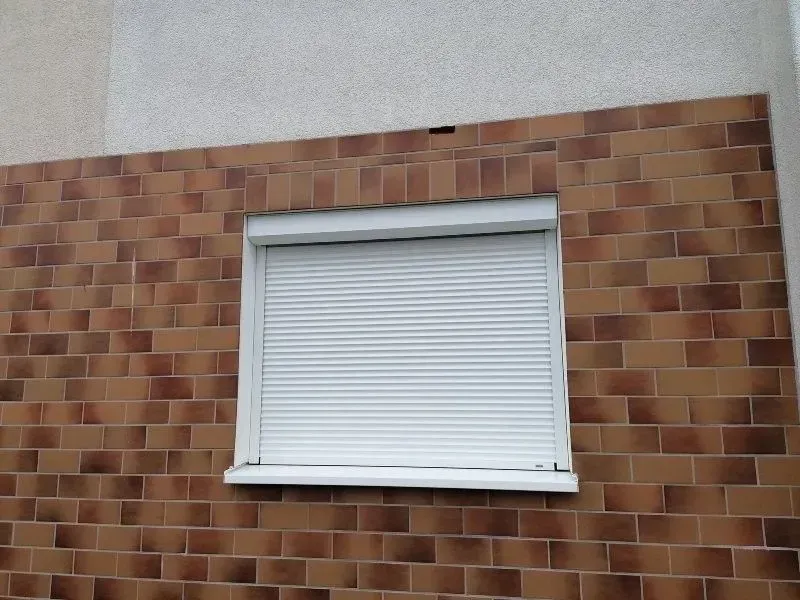 Fenster mit geschlossenen weißen Fensterläden an der Außenfassade eines Backsteingebäudes.