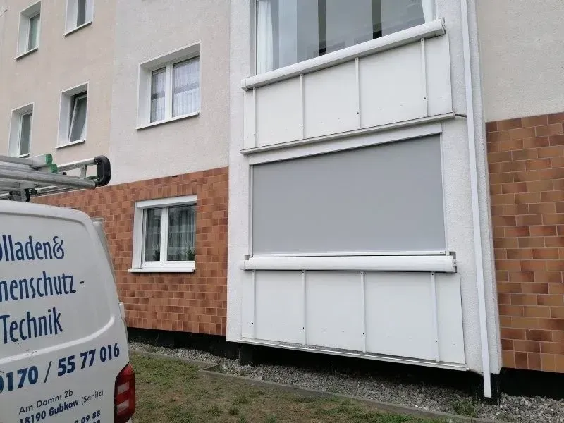 Ein Balkon mit grauem Sonnenschutz und ein Reparaturwagen mit der Aufschrift 