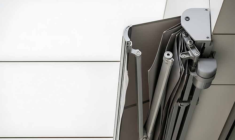 Zusammengefaltete, graue, einziehbare Markise an einem weißen Gebäude.