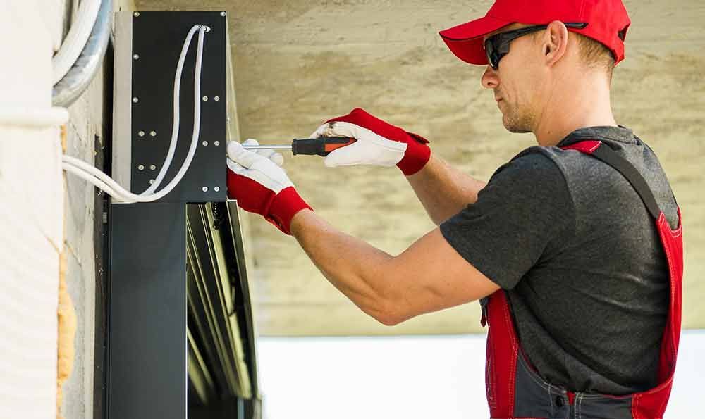 Person mit rotem Hut und Handschuhen befestigt im Freien einen schwarzen Gegenstand an einer Wand.