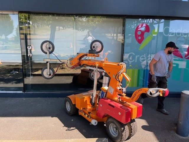 Un robot orange muni de ventouses soulève des vitres près d'un magasin