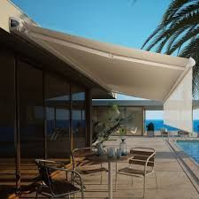 Un store rétractable beige protège une terrasse avec table et chaises, donnant sur une piscine