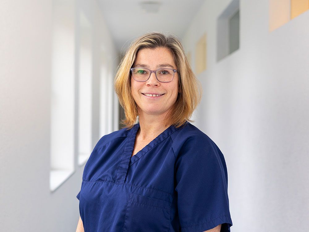 Eine Frau in einem blauen OP-Kittel und mit Brille steht in einem Flur.