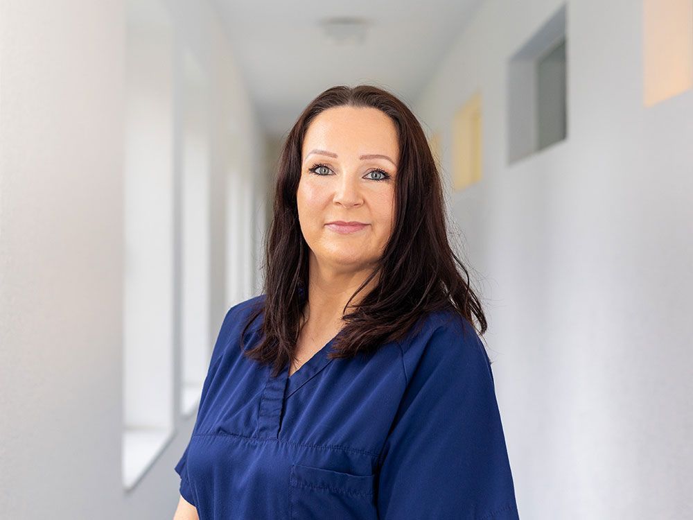 Eine Frau in einem blauen Kittel steht in einem Flur.