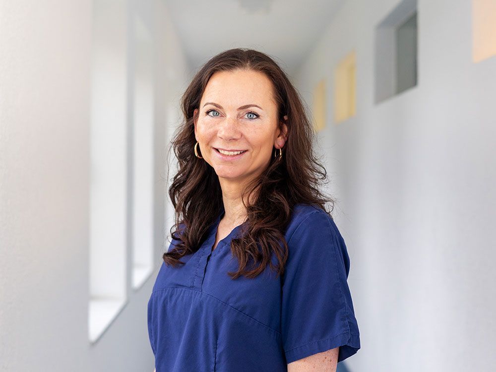 Eine Frau in einem blauen Kasack lächelt in einem Flur.