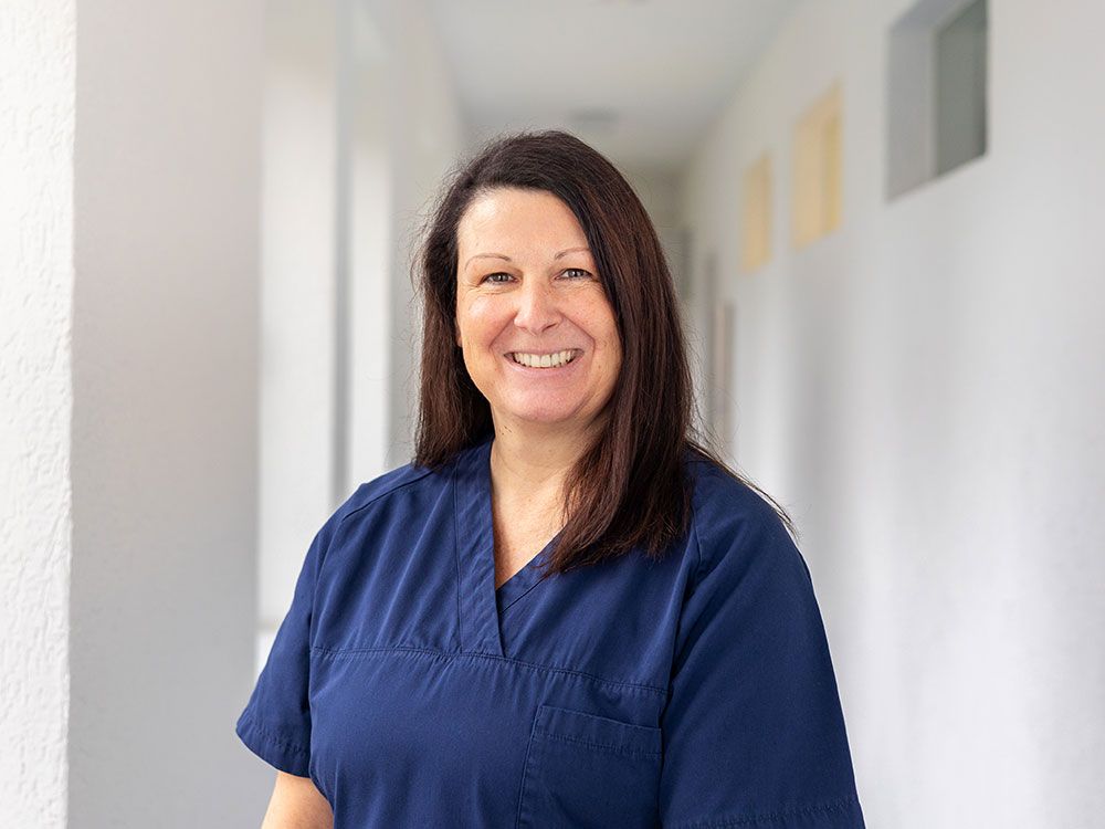 Eine Frau in einem blauen Kittel lächelt in einem Flur.