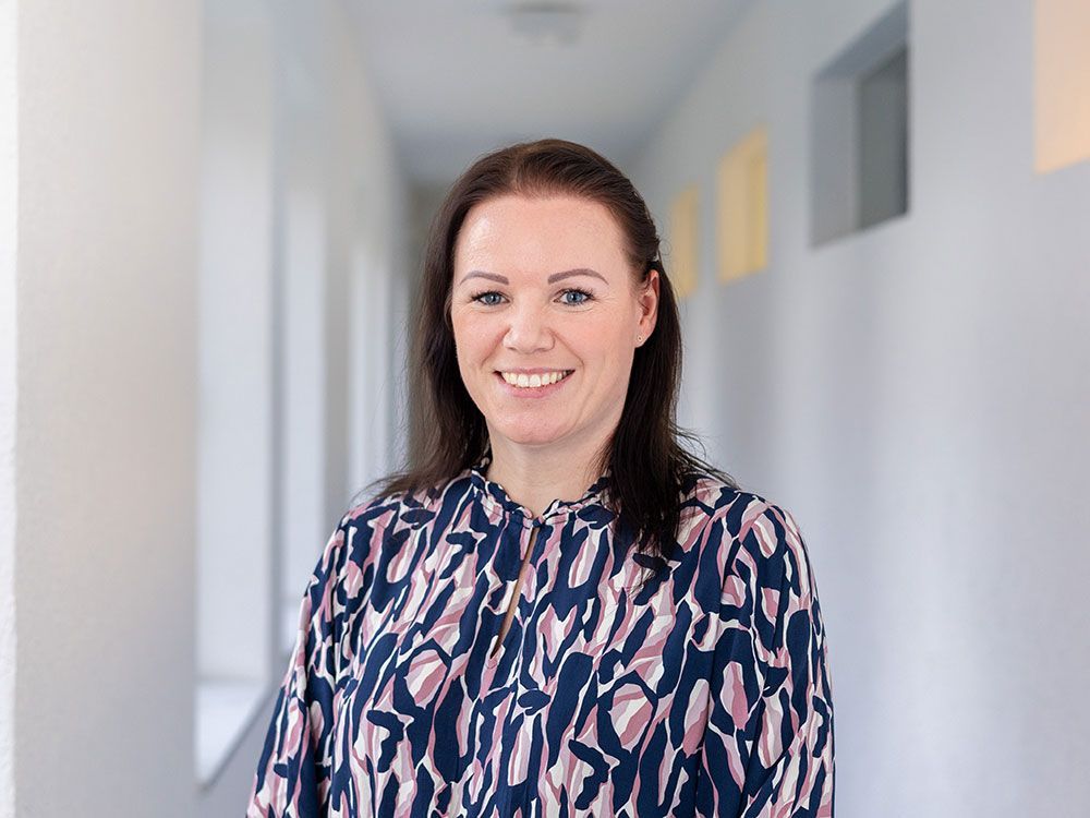 Eine Frau in einem Hemd mit Leopardenmuster lächelt in einem Flur.