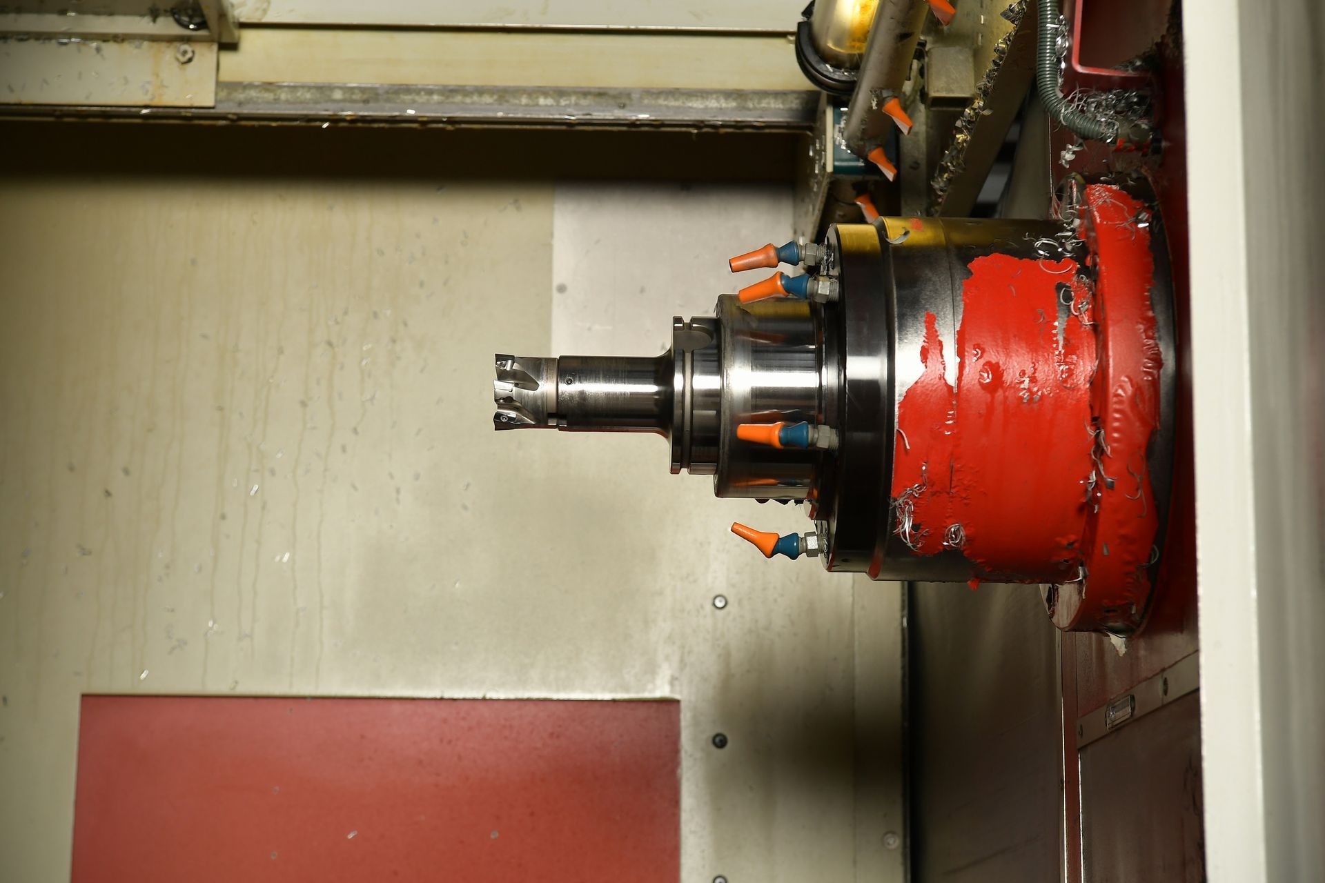 Eine Nahaufnahme des Spindelkopfes einer CNC-Maschine mit ausgefahrenem Schneidwerkzeug, bedeckt mit rotem Kühlmittel und Metallspänen.