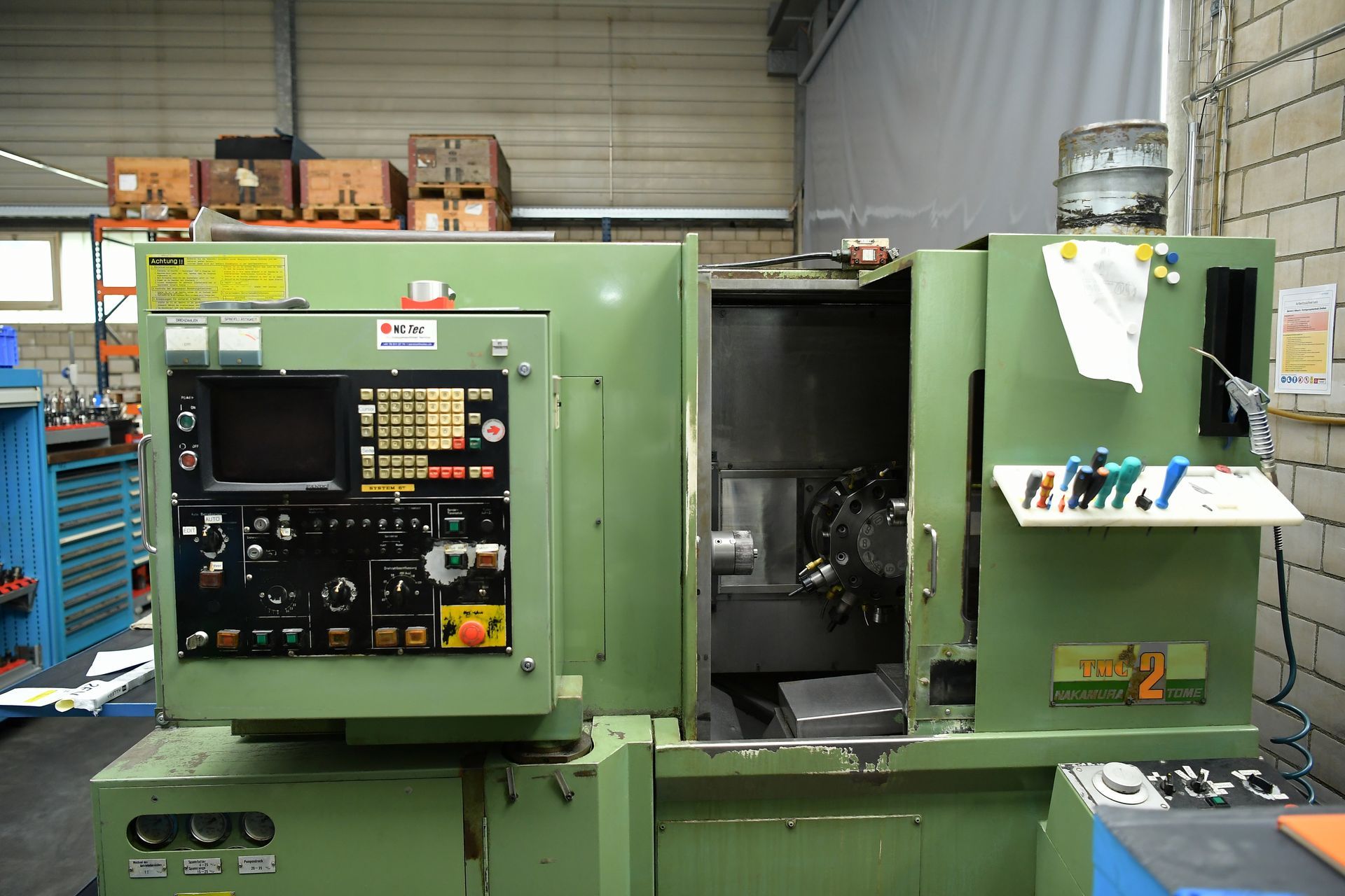 Grüne CNC-Maschine in einer Werkstattumgebung mit Bedienfeld und offener Tür.