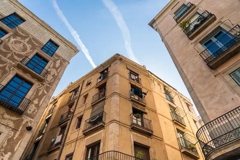 Edificios con balcones y ventanas, bajo un cielo azul con estelas de condensación.