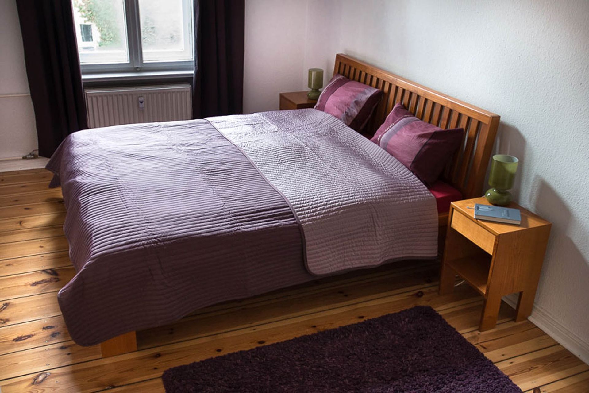 Ein weißer Heizkörper steht unter einem Fenster neben einer Kommode