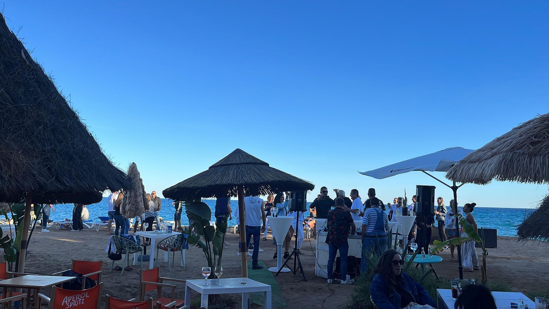 Puesta de sol sobre el océano con sombrillas de playa recortadas contra el cielo naranja y violeta brillante.