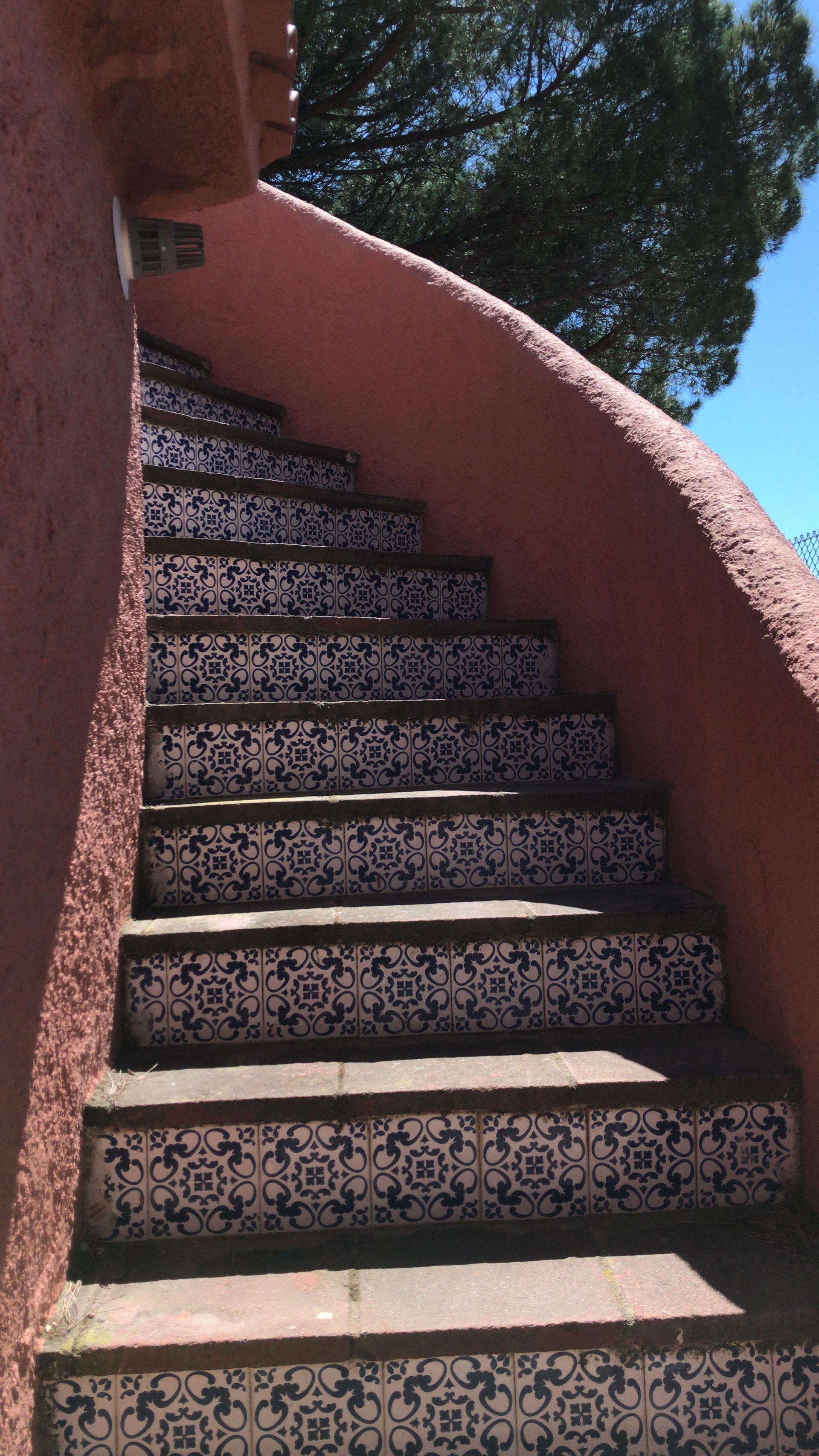 Escalera exterior con escalones de baldosas con dibujos azules y blancos, paredes rojas y cielo brillante.