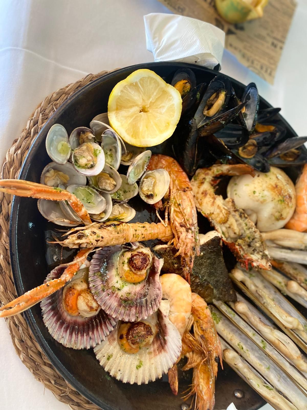 Plato de mariscos: almejas, mejillones, camarones, vieiras y navajas, servidos con limón.