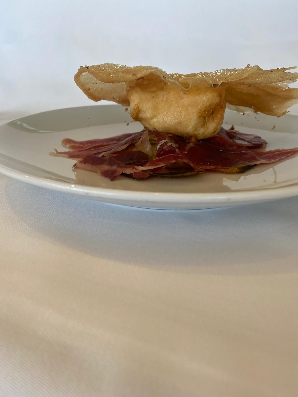 Plato gourmet con elementos fritos y crujientes, sobre carne en rodajas, en un plato blanco.