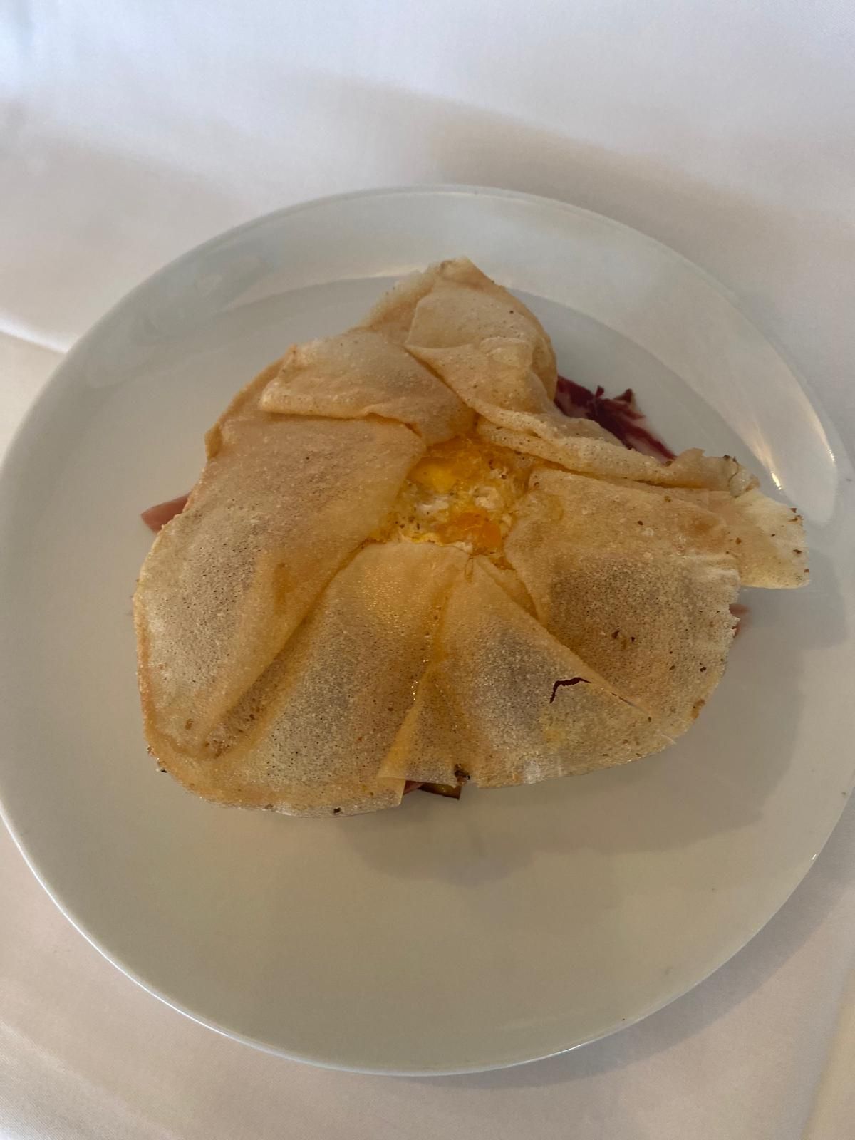 Pastel de desayuno en un plato blanco: sobre de masa de color marrón claro relleno de huevo y carne.