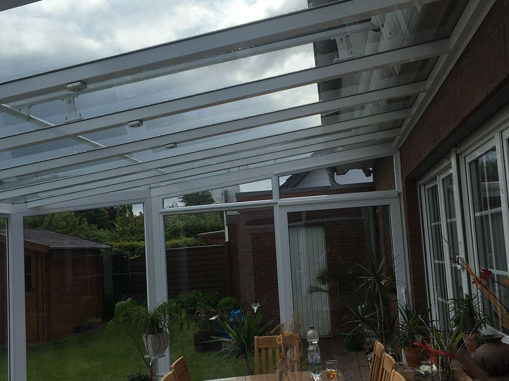 Eine Terrasse mit Tisch und Stühlen unter einem Glasdach