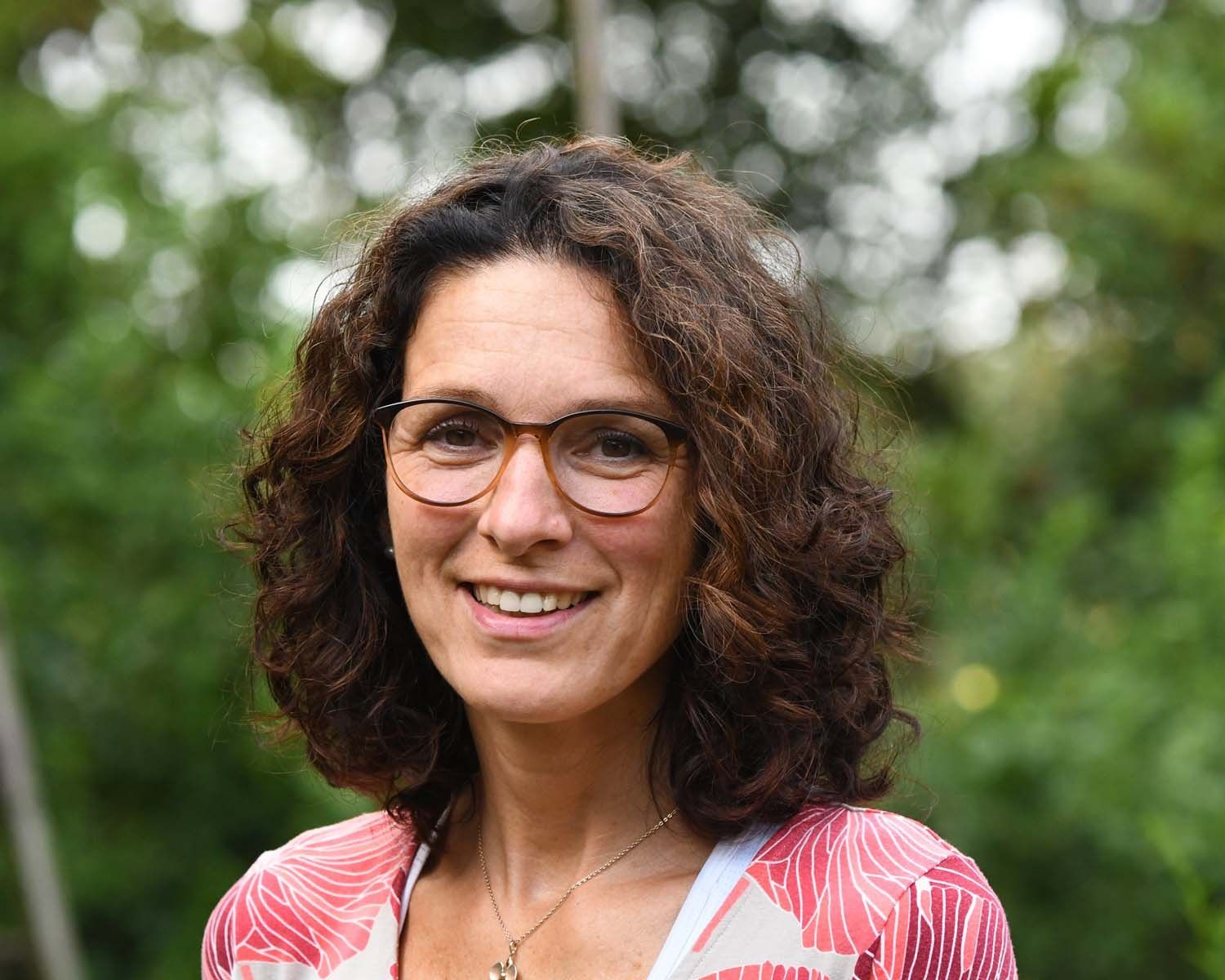 Eine Frau mit lockigem Haar und Brille lächelt in die Kamera.