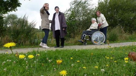 Eine Gruppe von Menschen geht neben einer Frau im Rollstuhl einen Weg entlang.