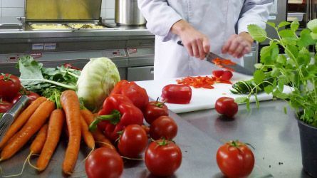 Ein Koch schneidet in einer Küche Gemüse auf einem Schneidebrett.