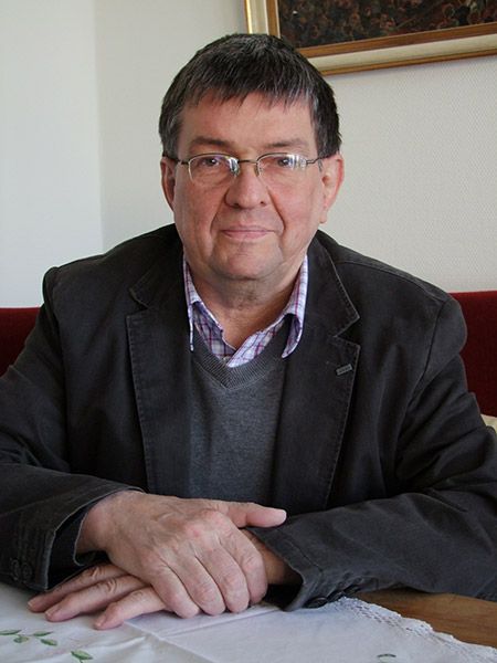 Ein Mann im Anzug sitzt mit gefalteten Händen an einem Tisch