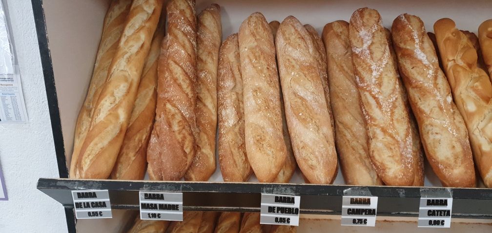 Baguettes en exposición en una panadería, varios panes dorados con etiquetas de precios.