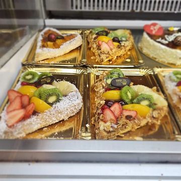 Rebanadas de tartaletas de frutas en una vitrina; fresas, kiwi, melocotones, uvas y otros aderezos sobre cortezas doradas.