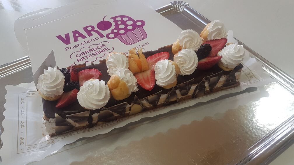 Pastel de chocolate con frutas y crema batida en una bandeja de plata, caja de panadería en el fondo.