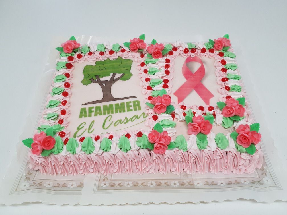 Pastel con glaseado rosa, decoraciones y un logo de árbol junto a una cinta rosa.