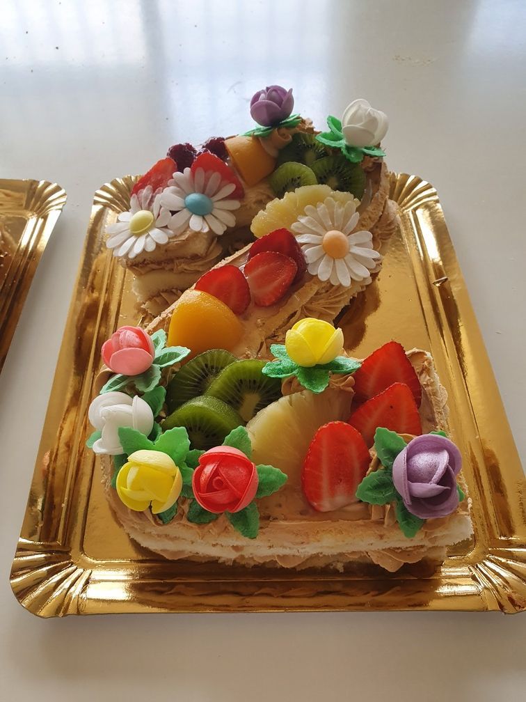Postre en forma de letra con decoraciones de frutas y flores en bandeja dorada.