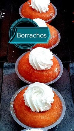 Cuatro borrachos cubiertos con crema batida, en recipientes de plástico transparente.