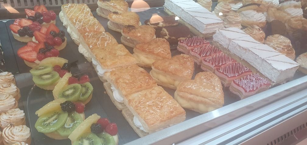 Vitrina repleta de pasteles variados, entre los que se incluyen tartas de frutas, pasteles rellenos de crema y productos horneados con forma de corazón.